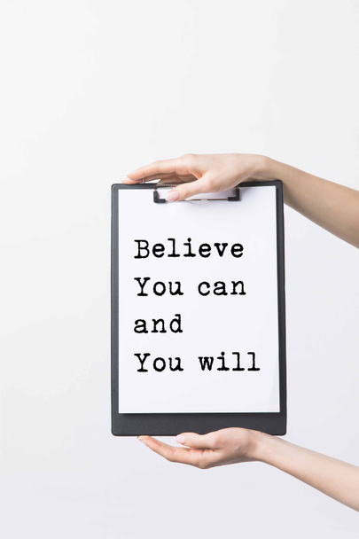 partial view of woman holding clipboard with "Believe You can and You will" inspiration in hands, isolated on white - Foto, afbeelding