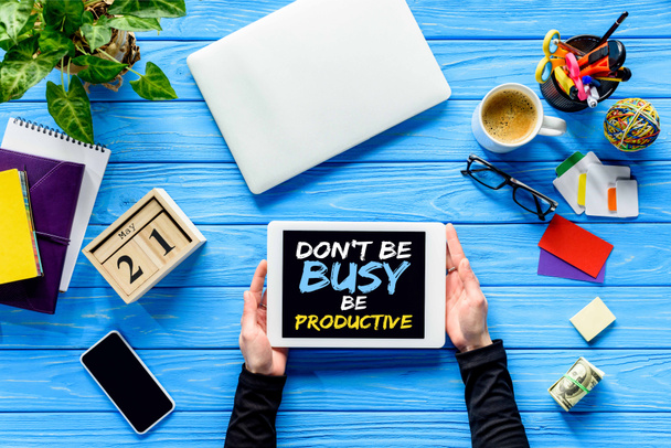 hands holding tablet on blue wooden table with money and stationery, Dont be busy be productive lettering  - Photo, Image