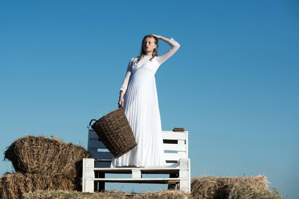 Sexy woman with long blond hair. Albino girl hold wicker basket with hay on sunny outdoor picnic. Woman bride in wedding dress on wooden bench. Fashion model on blue sky - Foto, Imagem