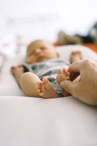 Les pieds du nouveau-né couchés dans les mains du bébé cocon et du père touchent doucement, faisant un massage doux
. - Photo, image