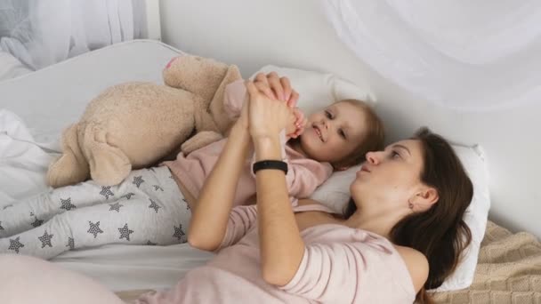 Mother and her little girl playing in the bed - Materiał filmowy, wideo