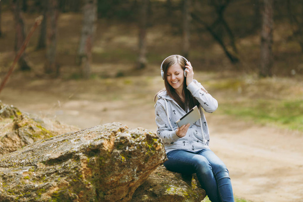 Młoda kobieta uśmiechający się w zwykłe ubrania, siedział na kamieniu, słuchanie - Zdjęcie, obraz