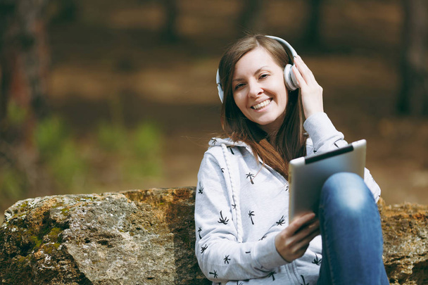 Joven mujer sonriente con ropa casual sentada en piedra escuchando
 - Foto, imagen
