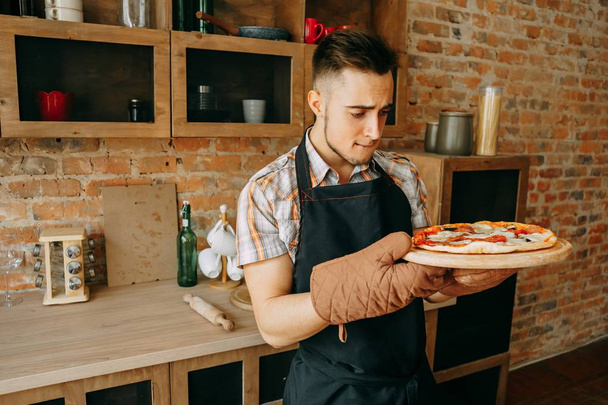 Young man unskilled cook look at self-cooked pizza - 写真・画像
