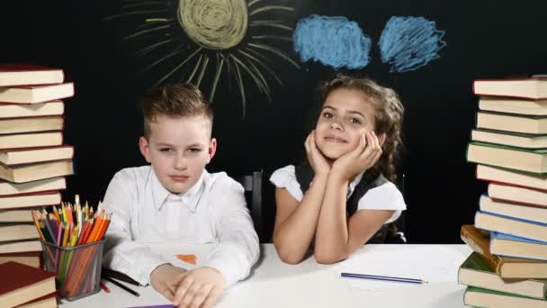 学校のコンセプトです。少年と少女は、書籍とその背後にある図面を黒板のヒープを持つ机に座る。子供たちは、楽しい時を過します。女の子は抱擁彼女の同級生です。4 k - 映像、動画