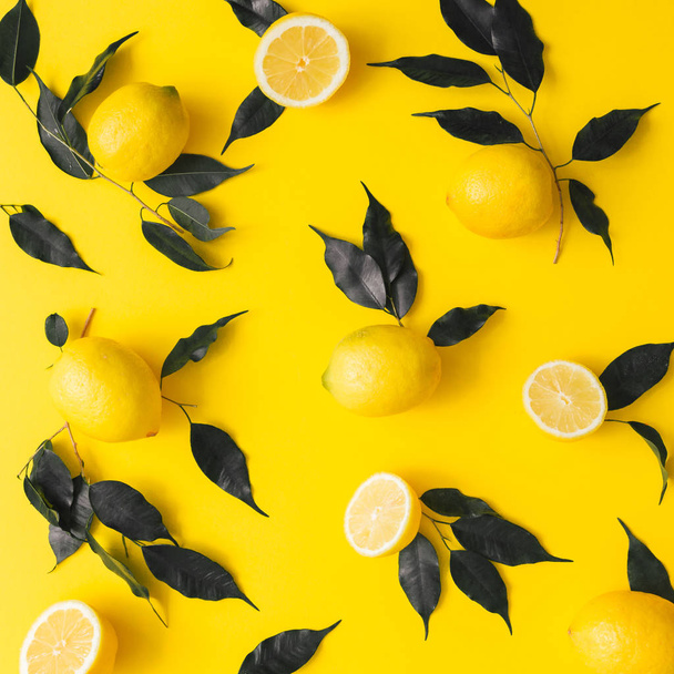 Creative summer pattern made of lemons and black leaves on yellow background. Fruit minimal concept. Flat lay. - Fotoğraf, Görsel