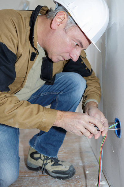 middle-age electrician repairing electrical socket on white wall - Foto, Imagem