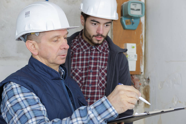 two male contractors holding clipboard by electric meter - Photo, image