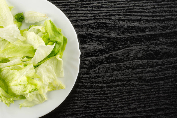 Iceberg lettuce fresh torn salad leaves on a white plate table top isolated on black wood backgroun - Fotografie, Obrázek