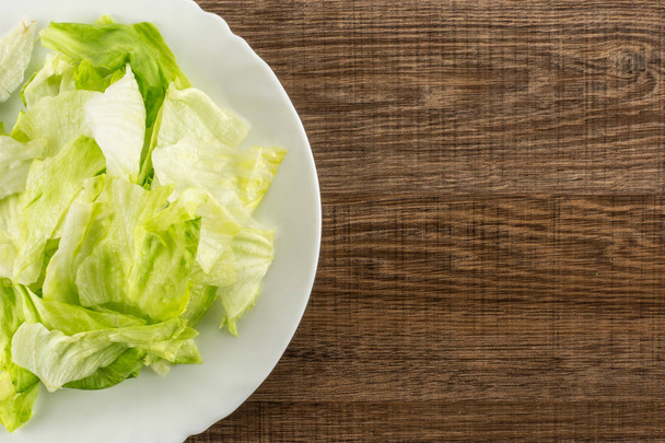 Iceberg lettuce fresh torn salad leaves on a white plate table top isolated on brown wood backgroun - Fotografie, Obrázek
