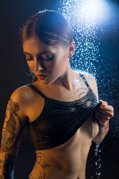 Young tattooed girl having shower in the dark - Photo, image