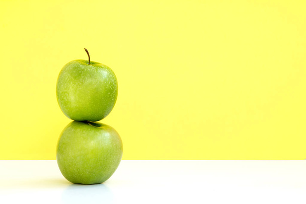 黄色の背景に別の 1 つの緑のリンゴ - 写真・画像