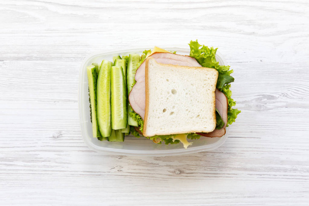 Lunch box con panino e verdure su sfondo bianco in legno, posa piatta. Dall'alto
.  - Foto, immagini