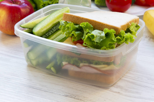 Lunchbox für die Schule mit Sandwich, Obst und einer Flasche Wasser auf weißem Holzhintergrund. Nahaufnahme. - Foto, Bild