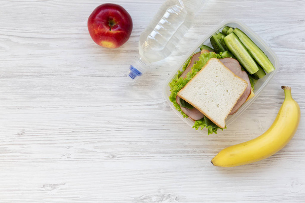 健康お弁当箱でサンドイッチ、フルーツ、白い木製の背景、フラットで水のボトルを置きます。上から。コピー スペース. - 写真・画像