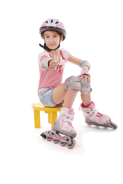 Charming broun-haired girl of school age in short jeans shorts and a pink t-shirt sitting on the chair and tries to foot roller skates. - Foto, imagen