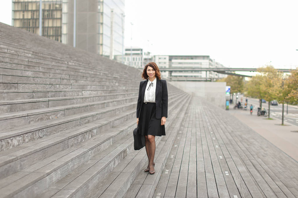 Kobieta stojąc na schodach z worka i wysokie budynki w tle. - Zdjęcie, obraz