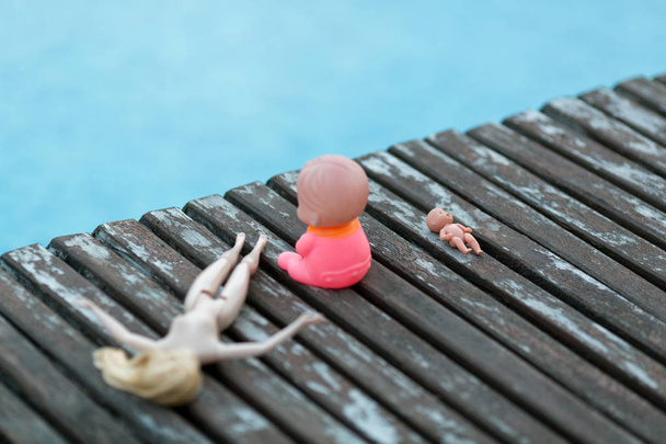 Vista de perto de três bonecas em tábuas de madeira perto da piscina
 - Foto, Imagem