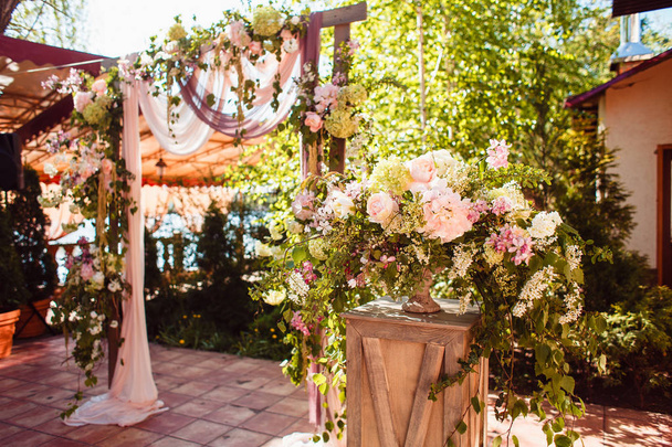 Flower composition on a wooden pedestal on the background of a wedding arch in rustic style - 写真・画像