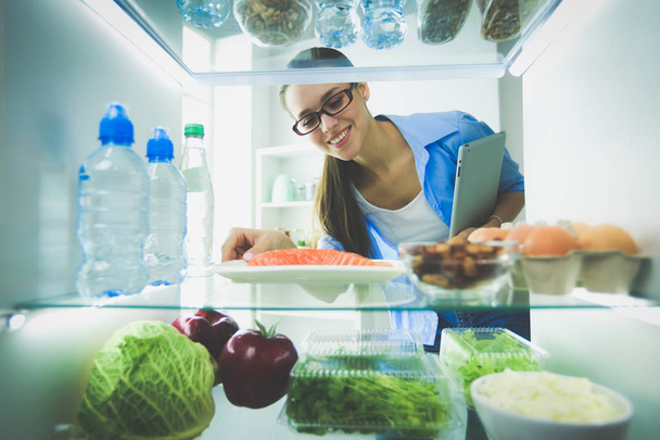 Portrait of female standing near open fridge full of healthy food, vegetables and fruits - Φωτογραφία, εικόνα