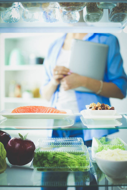 Portrait of female standing near open fridge full of healthy food, vegetables and fruits - Фото, зображення