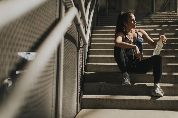 Portrait of pretty young female runner resting on stairs - Photo, image