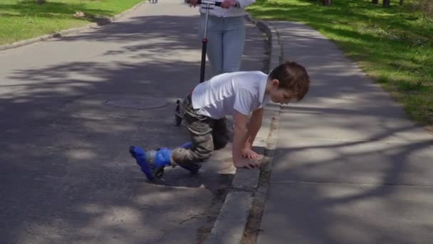 Little boy on roller skates rises to his feet after falling on the asphalt - Séquence, vidéo