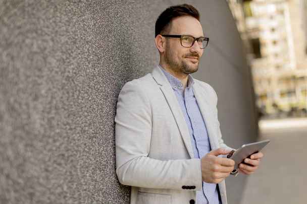 Bello giovane uomo d'affari con tablet digitale dal muro grigio
 - Foto, immagini