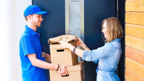 Smiling delivery man in blue uniform delivering parcel box to recipient - courier service concept. Smiling delivery man in blue uniform - Fotó, kép
