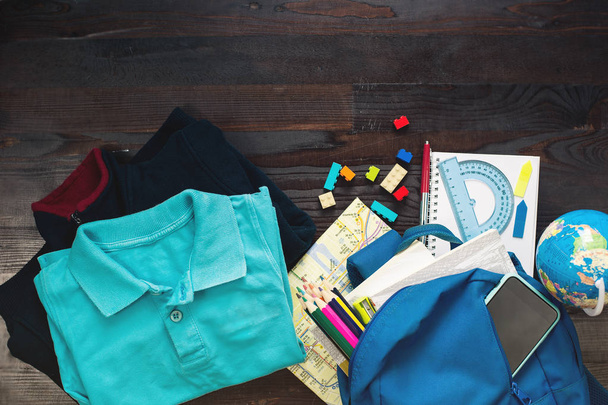 Concept of education. Top view school uniform, childrens, items in backpack and stationary on wooden background - Foto, immagini