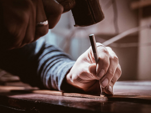 Close up of leather craftsman working with natural leather using hammer. Handbag master at work in local workshop. Handmade concept. Male shoemaker creating product with textile - 写真・画像