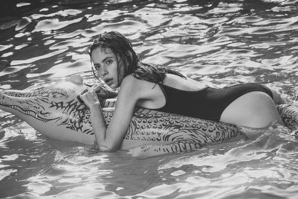 Fashion crocodile leather and girl in water. woman on sea with inflatable mattress. Relax in luxury swimming pool. Adventures of girl on crocodile. Summer vacation and travel to ocean, maldives - Foto, Imagem
