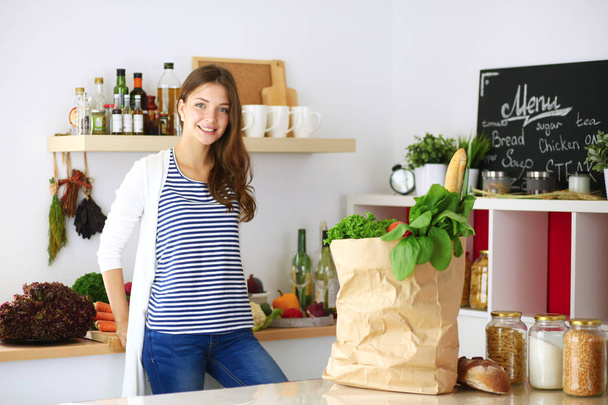 Young woman holding grocery shopping bag with vegetables .Standing in the kitchen. Young woman - Photo, image