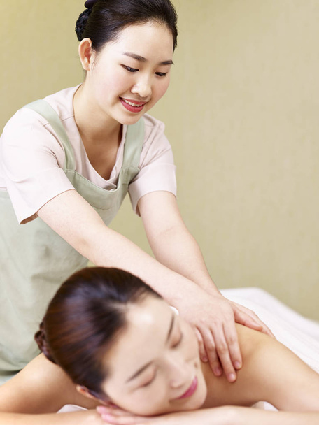 молодой азиатский массажист, выполняющий массаж женщины
 - Фото, изображение