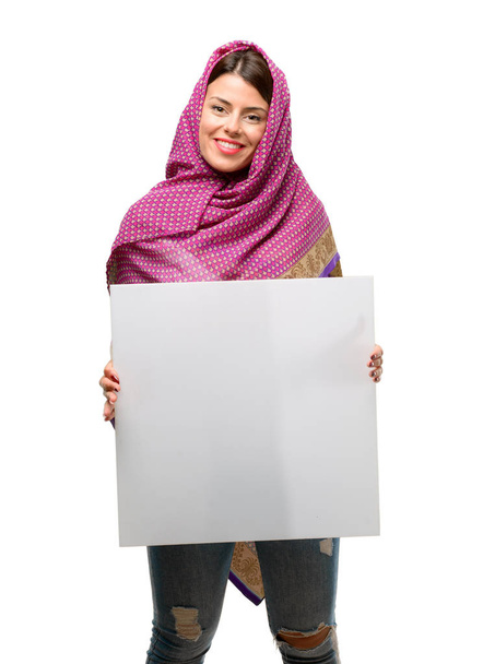 Young arab woman wearing hijab holding blank advertising banner, good poster for ad, offer or announcement, big paper billboard - Fotografie, Obrázek