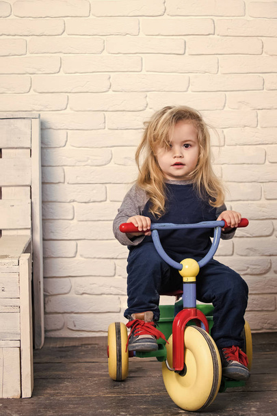 Baby cyclist with long blond hair on white brick wall - Zdjęcie, obraz
