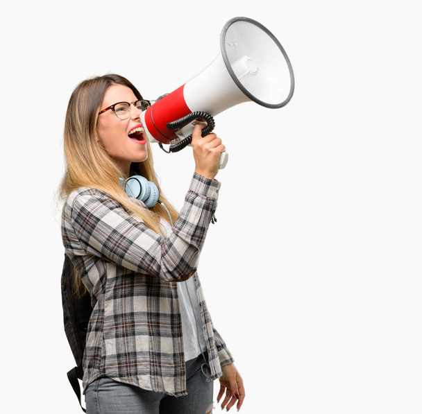 Jonge student vrouw met hoofdtelefoon en rugzak communiceert schreeuwen luid houden een megafoon, uitdrukken van succes en positieve concept, idee voor marketing of verkoop - Foto, afbeelding