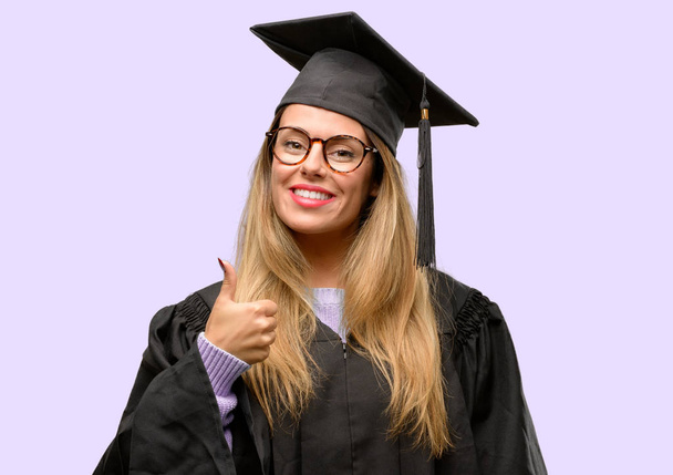 Νεαρή γυναίκα Πανεπιστήμιο μεταπτυχιακός φοιτητής που χαμογελάει σε γενικές γραμμές δείχνει μπράβο χειρονομία φωτογραφική μηχανή, την έκφραση της όπως και την έγκριση - Φωτογραφία, εικόνα