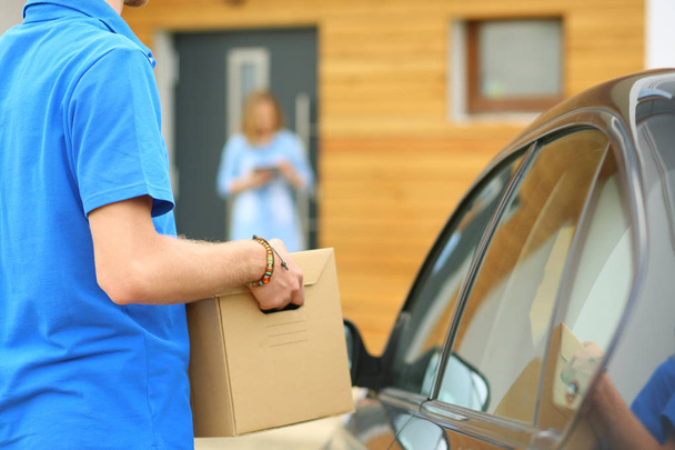 Smiling delivery man in blue uniform delivering parcel box to recipient - courier service concept. Smiling delivery man in blue uniform - Fotografie, Obrázek