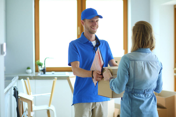 Homem de entrega sorridente em uniforme azul entregando caixa de encomendas ao destinatário conceito de serviço de correio. Sorrindo homem de entrega em uniforme azul - Foto, Imagem
