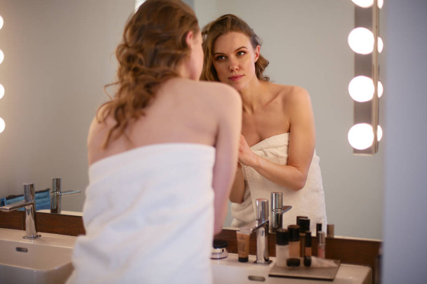 Молода жінка дивиться у дзеркало і одягає макіяж
. - Фото, зображення