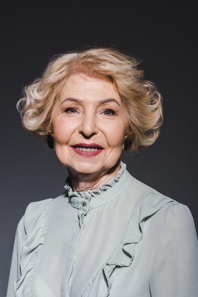 close-up portrait of smiling senior woman looking at camera on dark grey - Fotografie, Obrázek