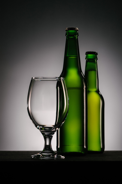 close up view of bottles of beer and empty glass on grey background - Fotografie, Obrázek