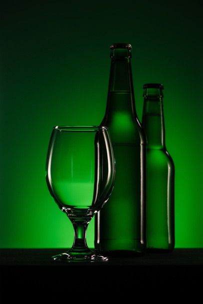 close up view of bottles of beer and empty glass on green background - Photo, image