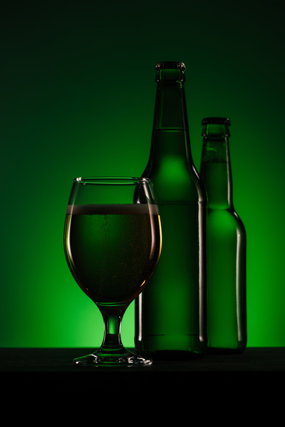 close up view of bottles and glass of beer on dark green background - Фото, изображение