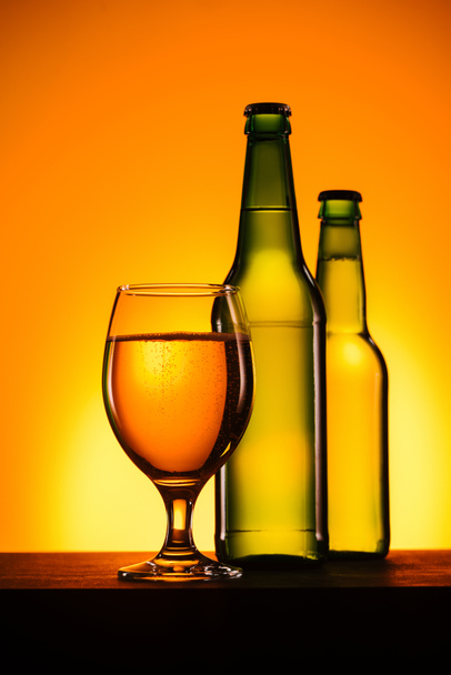 vista ravvicinata di bottiglie e vetro di birra sulla superficie su sfondo arancione
 - Foto, immagini