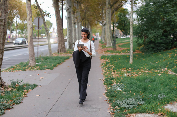 Афро американський молодий студент прогулянки з таблетку в Осінній Парк, носіння рюкзак. - Фото, зображення