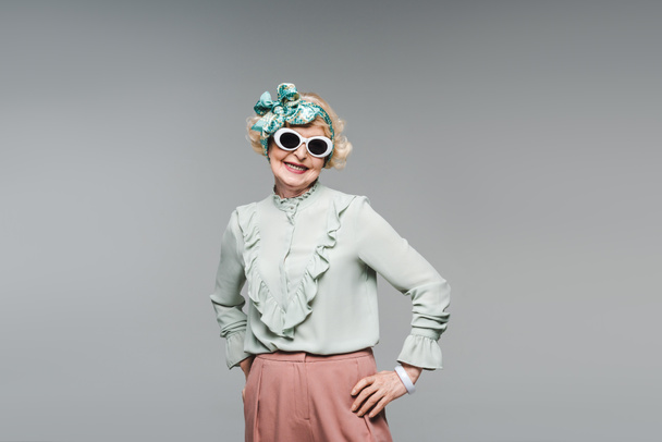 mulher sênior atraente na faixa de cabeça elegante e óculos de sol isolados em cinza
 - Foto, Imagem