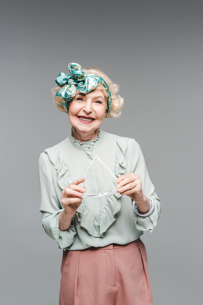 krásná starší žena v stylové oblečení drží brýle izolované Grey - Fotografie, Obrázek