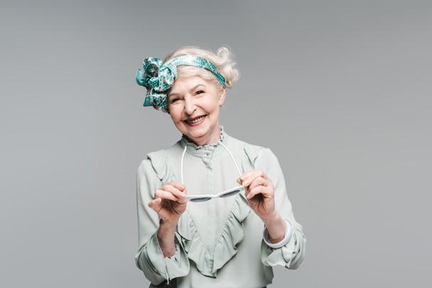 happy senior woman in stylish vintage clothes and sunglasses isolated on grey - Fotoğraf, Görsel